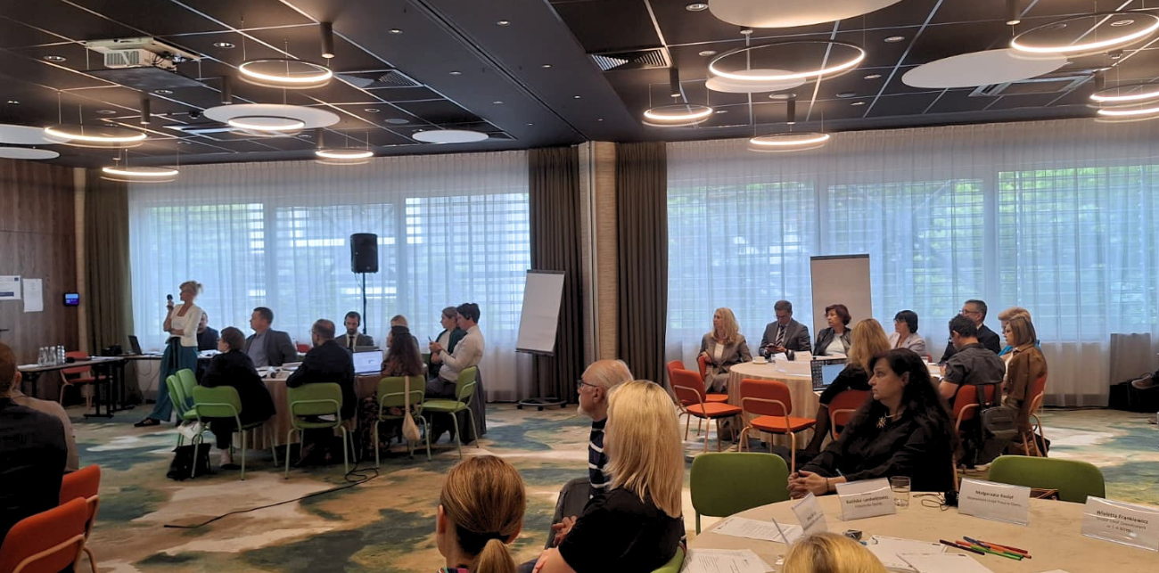 Uczestnicy spotkania siedzą przy stołach w sali konferencyjnej podczas warsztatów lub dyskusji grupowej.
