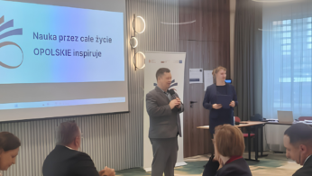 Dwóch prelegentów występuje przed uczestnikami konferencji; na ekranie widoczna jest prezentacja projektu.