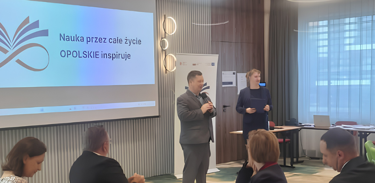 Dwóch prelegentów występuje przed uczestnikami konferencji; na ekranie widoczna jest prezentacja projektu.