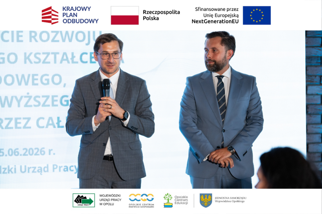 Dwaj mężczyźni w garniturach stoją na scenie przed dużym, jasnym ekranem z widocznym tekstem i datą 25.06.2026 r. Mężczyzna po lewej stronie trzyma mikrofon i przemawia, podczas gdy jego kolega po prawej słucha z rękami splecionymi przed sobą. Obraz zamykają białe pasy na górze i dole z logotypami m.in. Rzeczpospolitej Polskiej oraz Opolskiego Centrum Rozwoju Gospodarki.